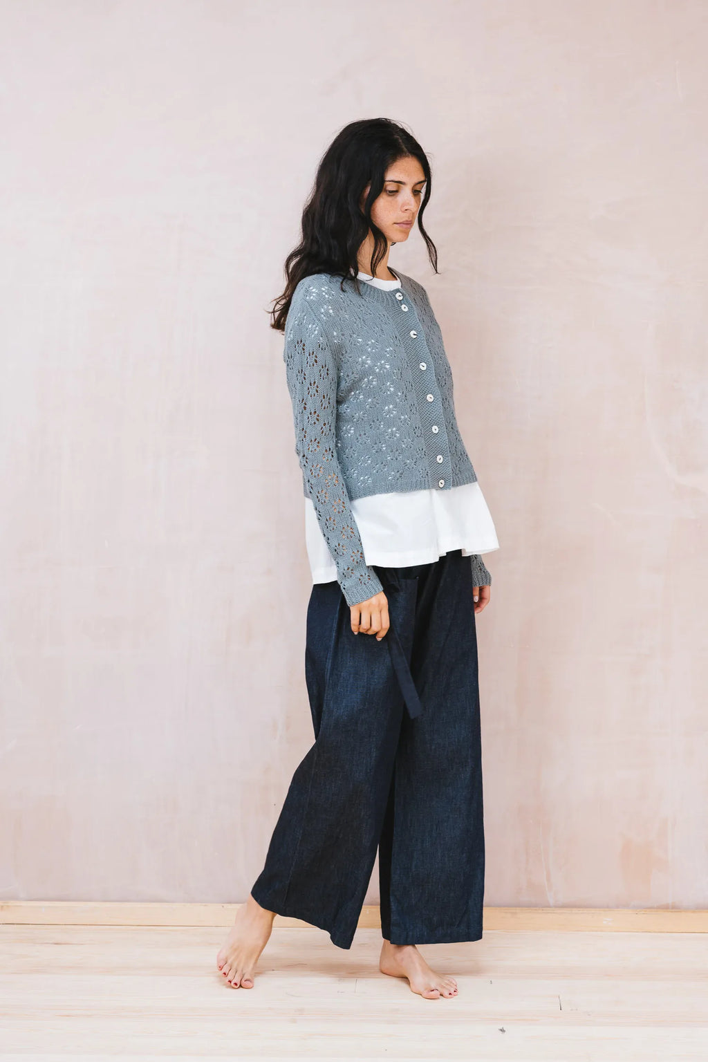 Woman wearing a layered outfit with a patterned top, white shirt, and dark pants against a plain background