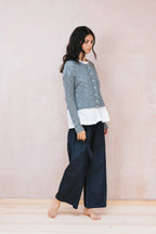 Woman wearing a layered outfit with a patterned top, white shirt, and dark pants against a plain background