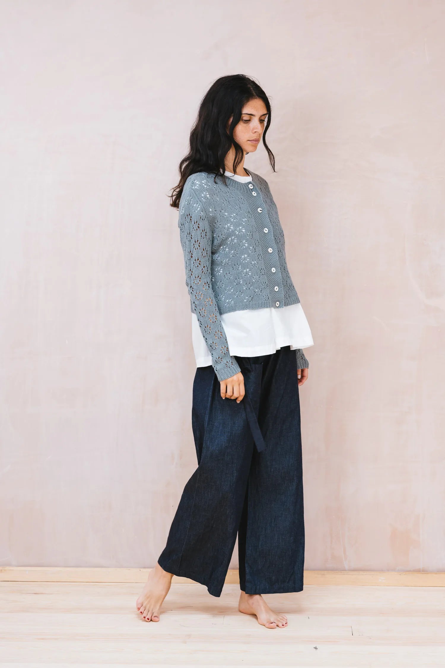 Woman wearing a layered outfit with a patterned top, white shirt, and dark pants against a plain background