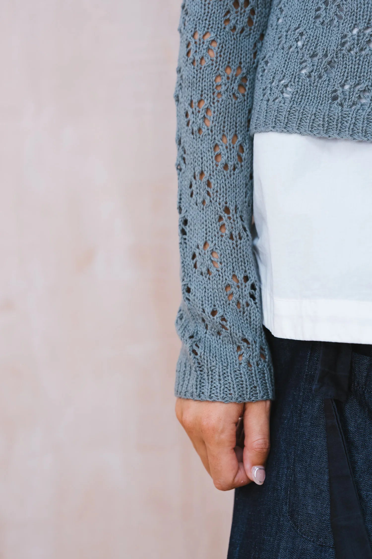 Close-up of a person wearing a blue knitted sweater with a white shirt underneath.