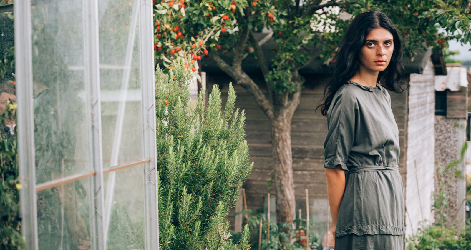Woman in a green dress standing in a garden with trees and plants around her.